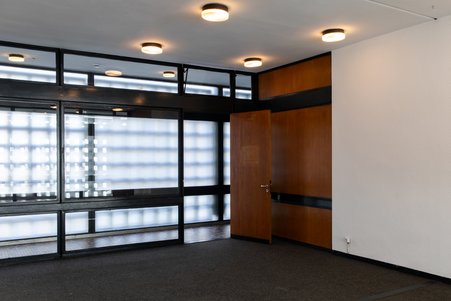 Das Foto zeigt das Foyer-Gebäude von innen mit seinen gläsernen Wänden und Holzvertäfelungen. 