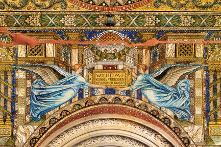 Auf diesem Foto wird ein Detail von dem Wandmosaiken gezeigt. Man sieht zwei Engel, die eine Tafel mit der Aufschrift "Wilhem I." zeigen.
