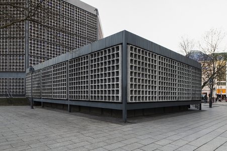 Das Foto zeigt das Foyer-Gebäude von außen: ein kleines Flachdachgebäude mit den typischen Betonwabenfassaden.