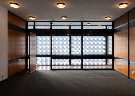 Fas Foto zeigt das Foyer von Innen mit seinen Glasfenstern und den Schattenrastern von den äußeren Betonwaben.