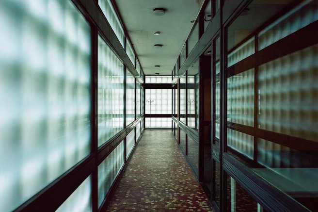 Das Foto zeigt das Foyer von innen mit seinen großen Milchglasfenstern, auf denen sich das Raster der Betonwaben als Schatten abbildet.